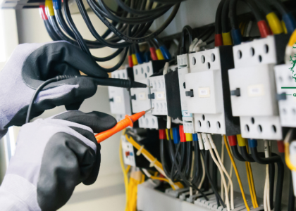 Electrician in protective gloves testing circuit breakers in a distribution board with a test probe, representing Electrician training at Artisan Training Institute