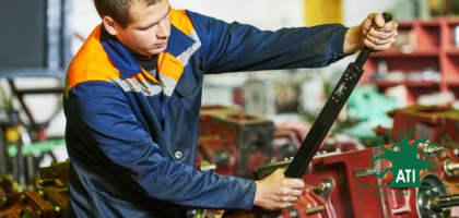 Fitter and Turner apprentice in blue overalls using a long torque wrench on a machine assembly in a workshop, representing a Fitter and Turner career