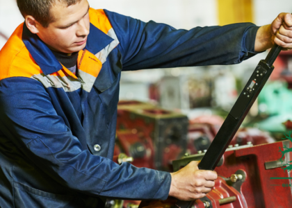Fitter and Turner apprentice in blue overalls using a long torque wrench on a machine assembly in a workshop, representing a Fitter and Turner career