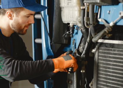 Heavy equipment mechanic in a cap and safety gloves using a spanner to service a machine engine, representing a Heavy Equipment Mechanic career