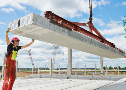 Two riggers in red overalls and hard hats guiding a concrete slab lifted by a crane, Artisan Training Institute