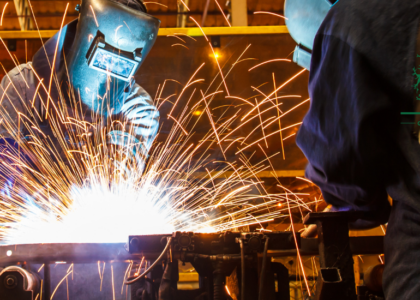 Two welders in protective helmets welding steel in a workshop, starting a welder career